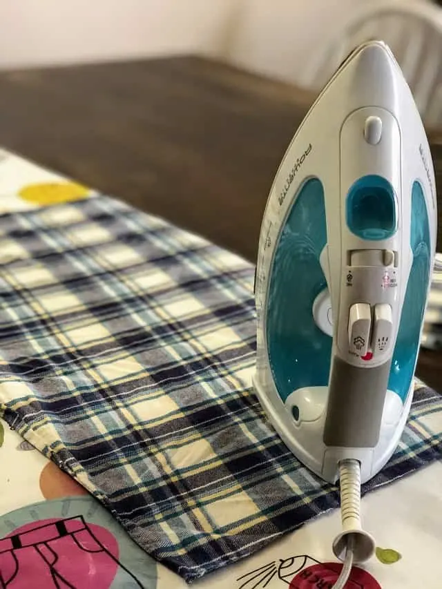 An iron sitting on top of a piece of flannel on an ironing board.