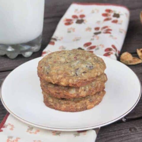 3 coconut chocolate chip cookies on a plate with a glass of milk and a napkin.