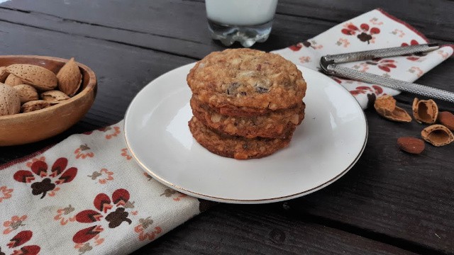 Coconut chocolate chip cookies on a plate with a bowl of almonds, napkin, nutcracker, and glass of milk.