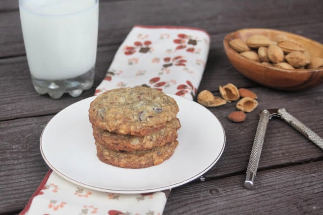 Coconut chocolate chip cookies on a plate with a bowl of almonds, a few almond shells, a napkin, nutcracker, and glass of milk.