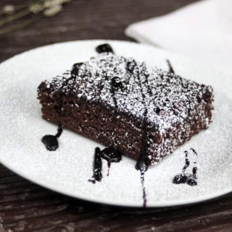 Lavender chocolate syrup brownie on a plate dusted with powdered sugar and chocolate syrup.