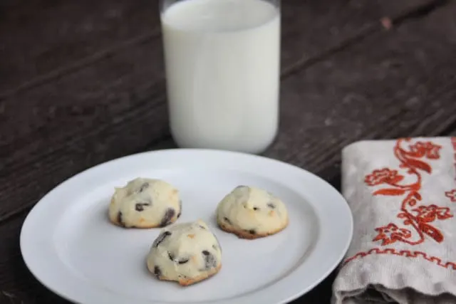 3 orange chocolate chip cookies on a plate with napkin and glass of milk.