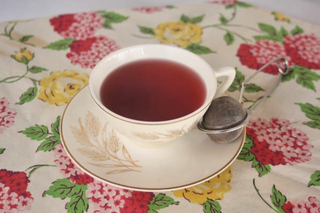 A cup of red tea on a saucer with tea ball. 