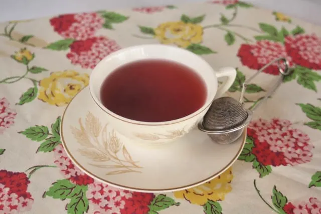 A cup of red tea on a saucer with tea ball. 