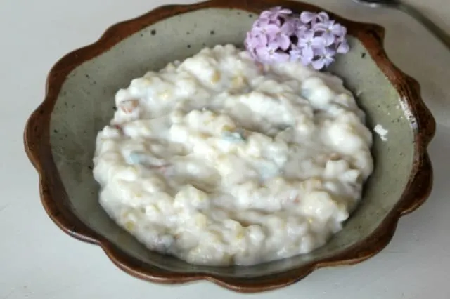 A bowl of lilac rice pudding garnished with a branch of fresh lilac blossoms.