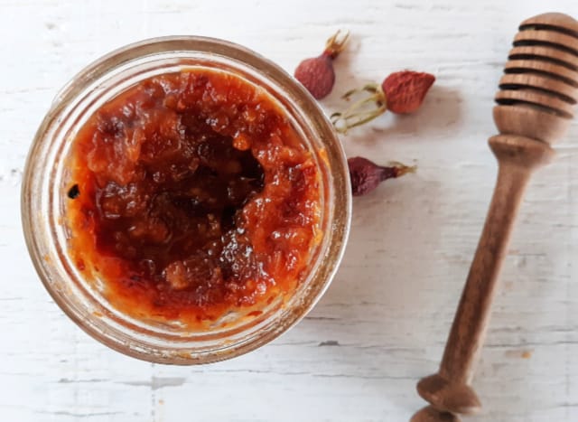 A jar of dried fruit and rosehip jam surrounded by honey dipper and dried rosehips. 