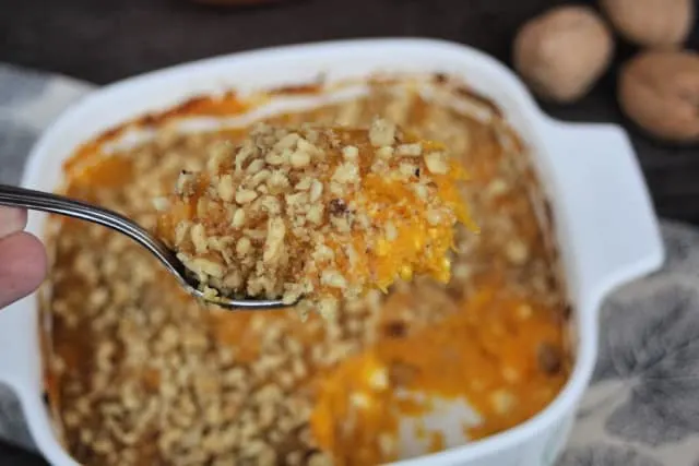 A spoonful of pumpkin casserole held above the pan.