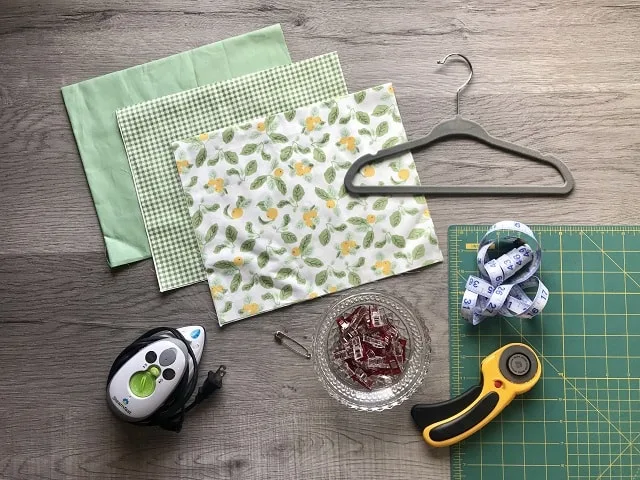 Green and yellow fabric, hanger, iron, sewing clips and rotary cutter