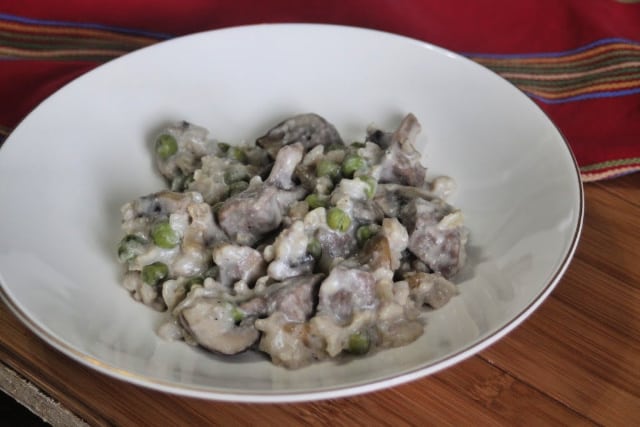 Beef casserole with rice, mushrooms, and peas in a white bowl.