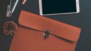 A leather satchel, pens, and smart phone on a dark table top with text overlay.