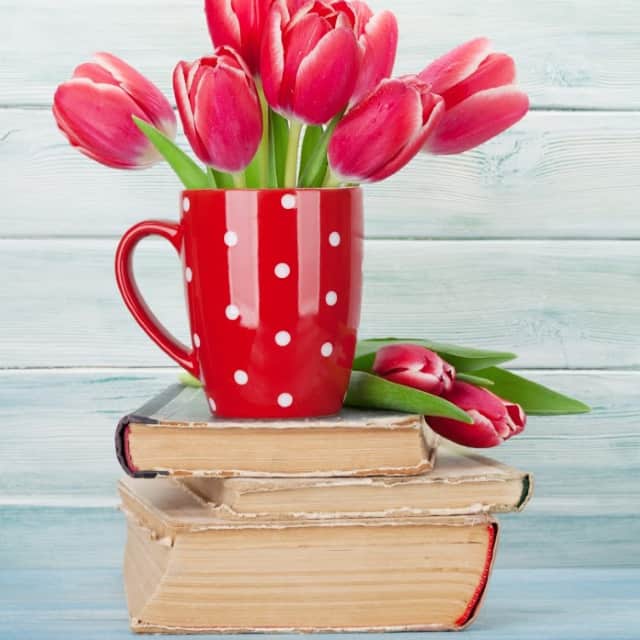 A red and white polka dotted coffee mug full of tulips sitting on top of a stack of old books.
