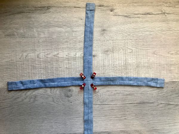 Two strips of fabric laying on top of one another perpendicular in the center, held with sewing clips