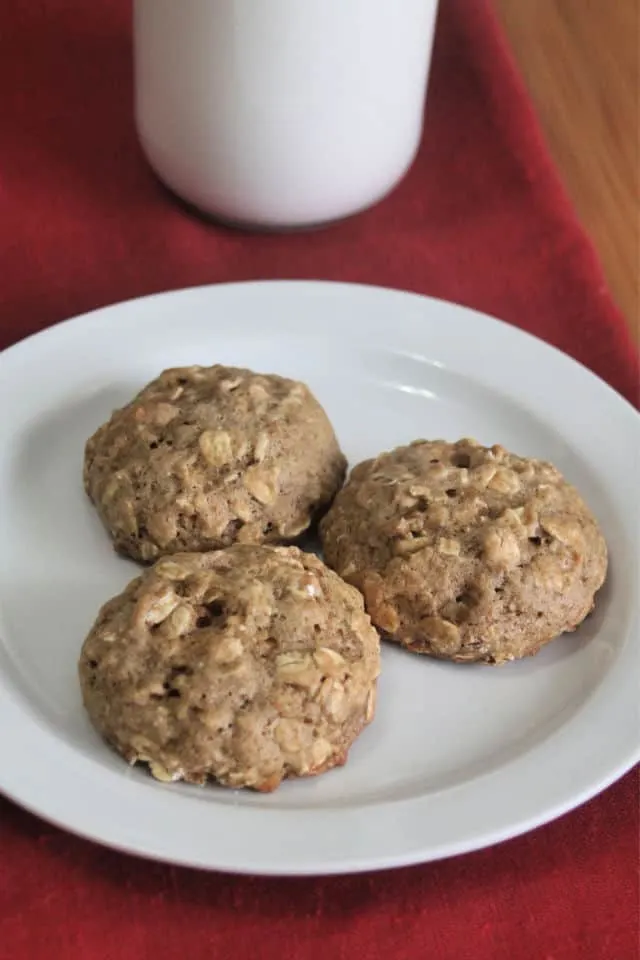 Applesauce oatmeal cookies on a plate with a glass of milk.