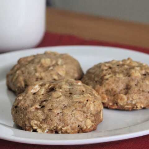 Applesauce cookies on a white plate with a glass of milk in background.