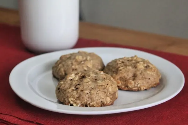 Applesauce oatmeal cookies on a plate with a glass of milk.