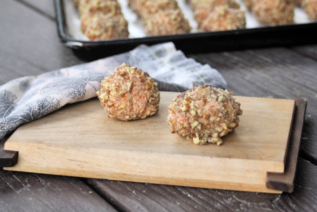 2 frozen sweet potato balls on a wooden board with a napkin and tray of frozen balls in the background.