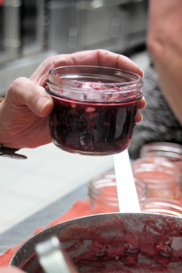 A woman's hand holding a canning jar full of cherry jam.