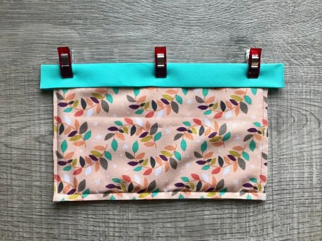 Double fold bias in teal color clipped across top of fabric rectangle and batting sandwich