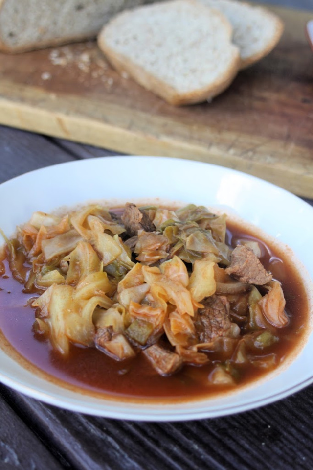 A bowl of beef and cabbage stew with slices of bread on a table