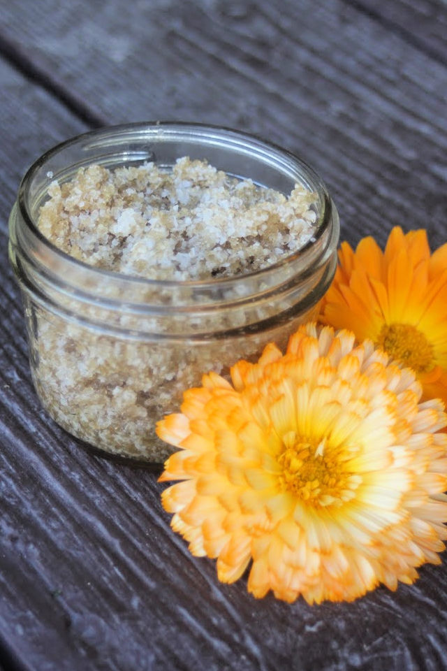 An open jar of calendula sugar scrub surrounded by fresh calendula flowers.