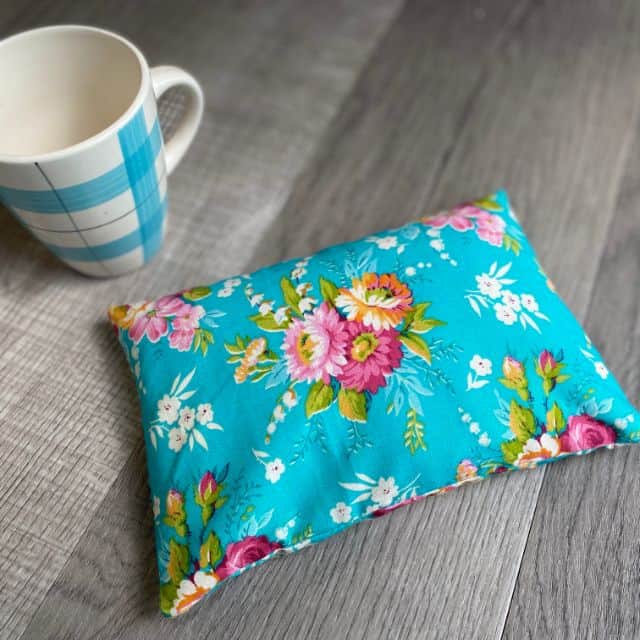 A floral rice-filled heating pad sitting on a table by a coffee cup.