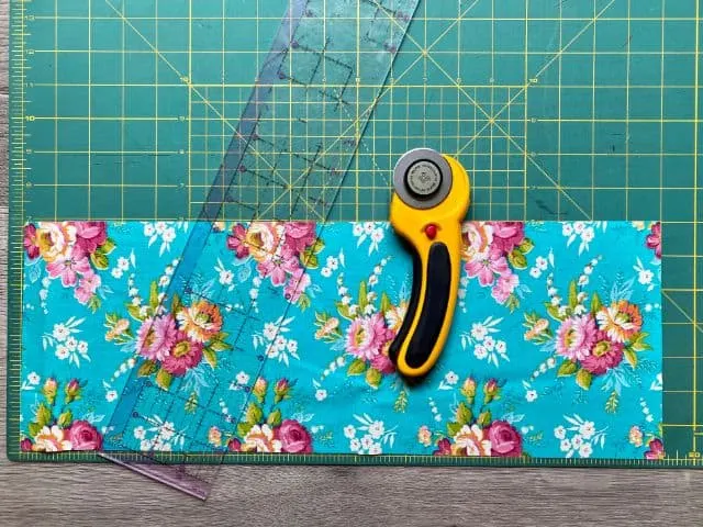 Teal floral fabric laying on cutting mat with rotary cutter and ruler