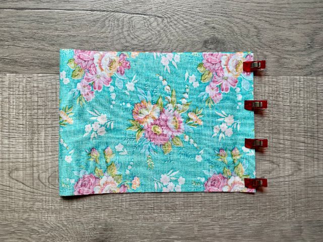 Teal floral fabric folded in half with sewing clips holding open end