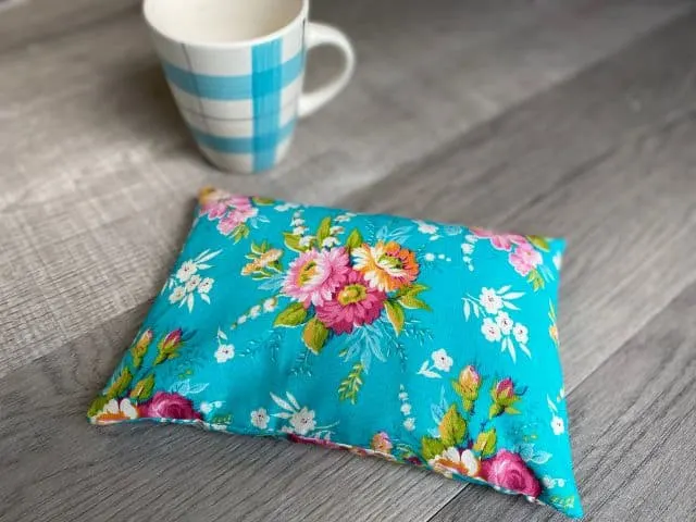 Teal floral fabric rectangle pouch filled with rice and coffee mug flat lay
