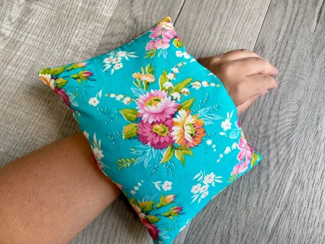 Teal floral fabric rectangle pouch filled with rice laying across wrist