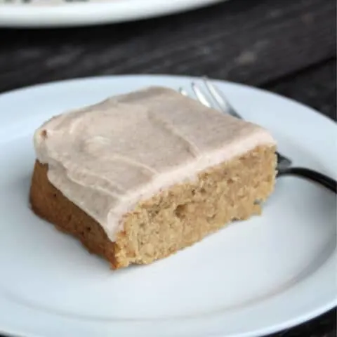 An apple butter bar with cinnamon frosting on a white plate with a fork.