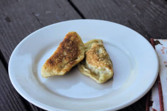 2 fried bacon cabbage pierogies on a white plate sitting next to a napkin.