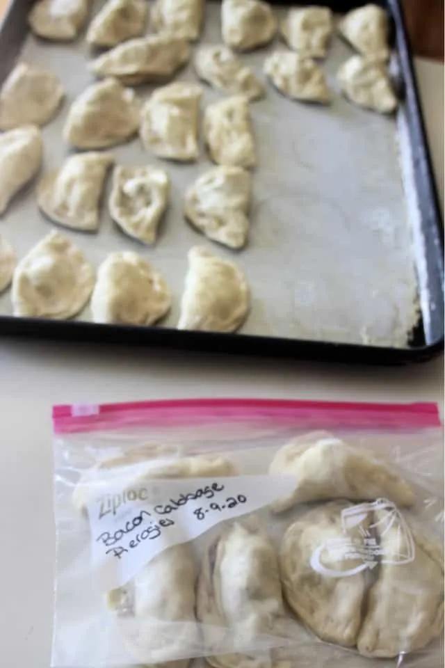 A plastic bag full of frozen bacon cabbage pierogies sitting in front of a cookie sheet full of more frozen pierogies.