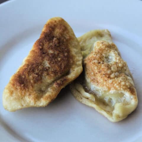 2 fried bacon cabbage pierogies on a white plate.