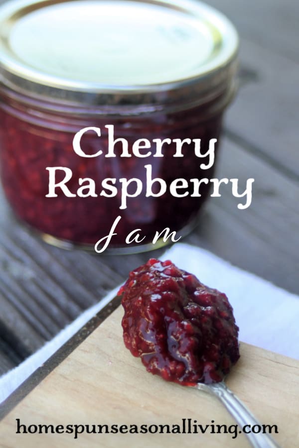 A spoon heaped with cherry raspberry jam on a wooden board with a sealed jar behind it with text overlay. 