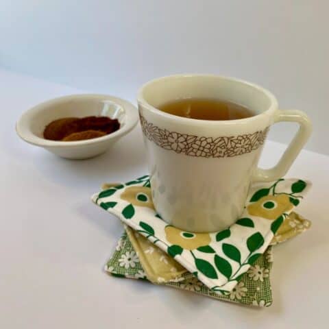 Tea in white coffee mug setting on three fabric mug rugs with a bowl of spices in background