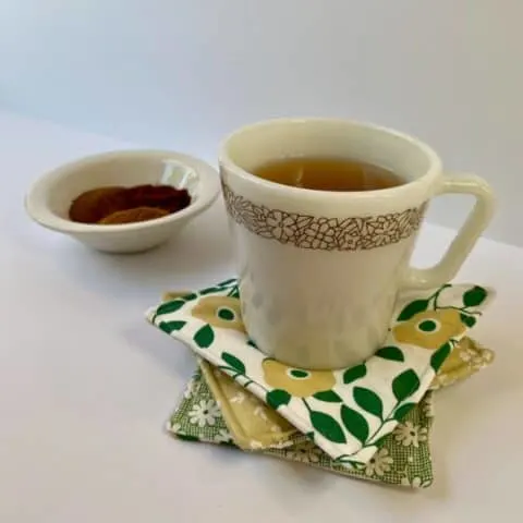 Tea in white coffee mug setting on three fabric mug rugs with a bowl of spices in background