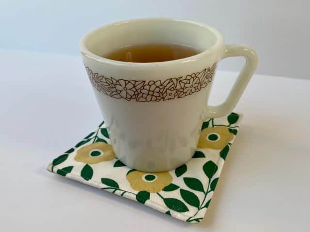 White mug of tea setting on green flowered mug rug