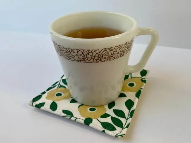 White mug of tea setting on green flowered mug rug