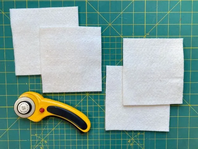 Four squares of batting on cutting mat with rotary cutter