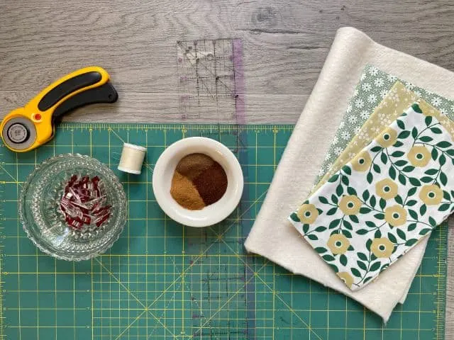 Flat lay of cutting mat, rotary cutter, sewing clips, thread, ruler, spices, batting and fabric