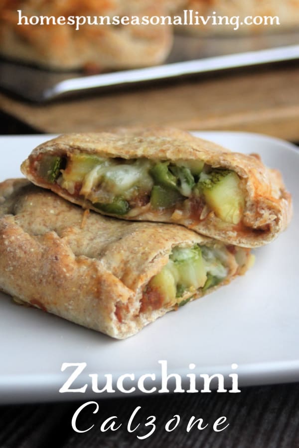 A calzone sitting on a plate that is cut in half, exposing the filling on a white plate with text overly stating: Zucchini Calzone. 