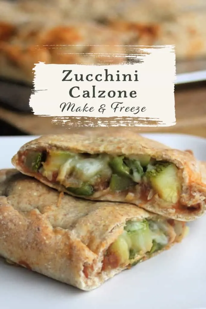 A zucchini calzone sliced in half exposing the vegetables inside the dough on a white plate with text overly stating zucchini calzone make & freeze.