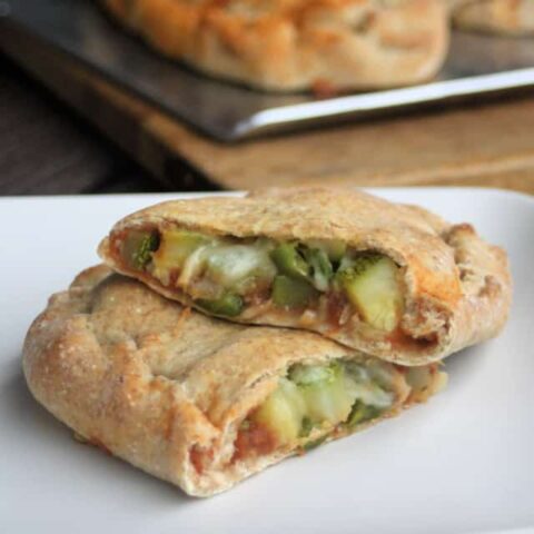 A zucchini calzone sliced in half exposing the vegetables inside the dough on a white plate.