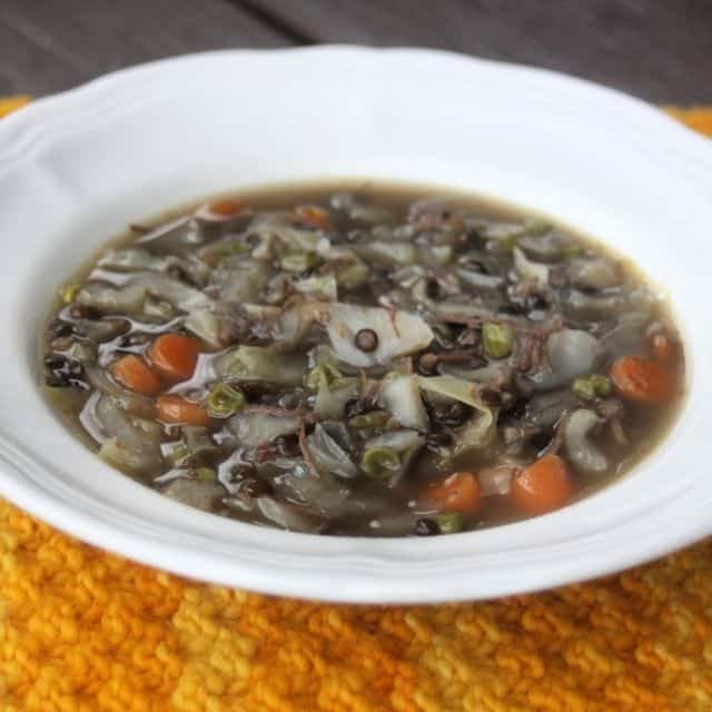 A white bowl full of cabbage lentil soup sitting on an orange table runner.