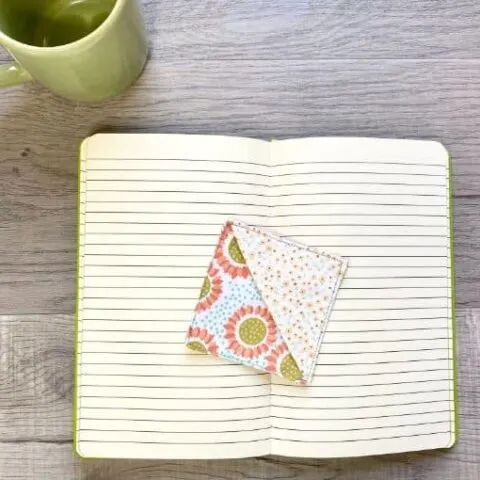 Mug and open book with square fabric corner bookmark laying in center