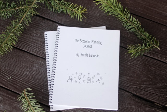 Two coil bound seasonal planners sitting on a table surrounded by evergreen branches.