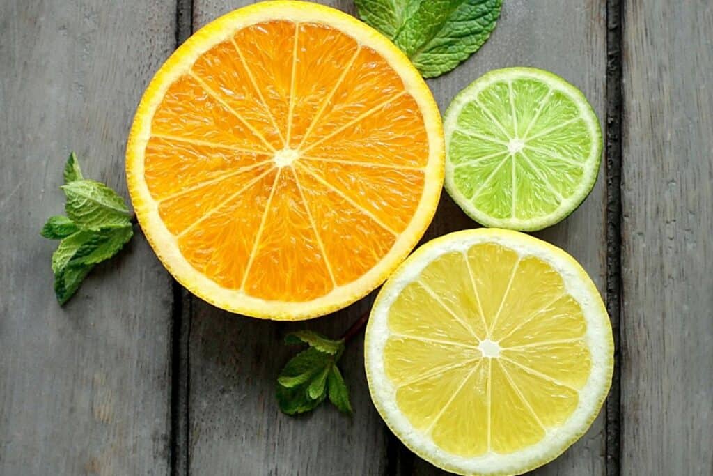 Slices of an orange, a lime, and a lemon on a table showing the interior segments of the fruit.