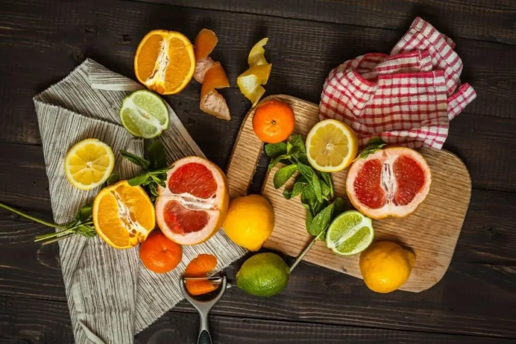 A variety of citrus whole and cut in half on a wooden board and linens scattered on a table.