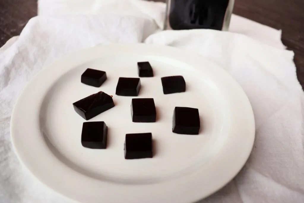 Elderberry syrup gummies in square shapes on a white plate sitting on a white linen.