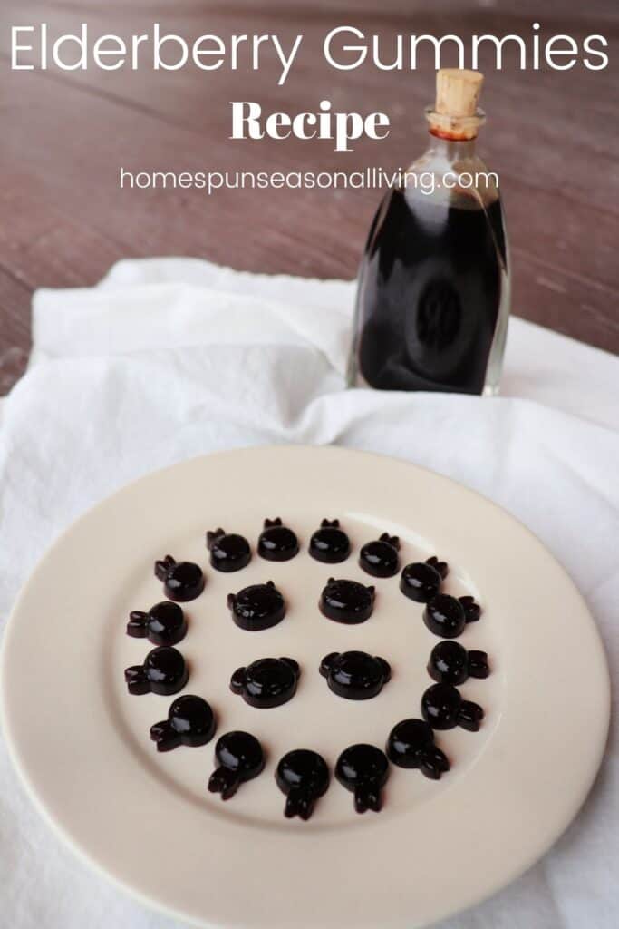 Purple gummies in animal shapes arranged on a white plate sitting on a white linen with a bottle of syrup in the background with text overlay reading: Elderberry Gummies Recipe.